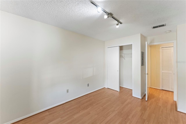 unfurnished bedroom featuring visible vents, baseboards, light wood-style floors, a closet, and a textured ceiling