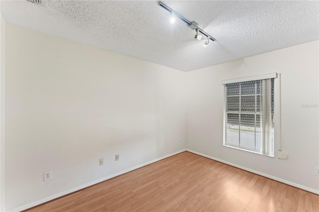 unfurnished room featuring rail lighting, wood finished floors, baseboards, and a textured ceiling