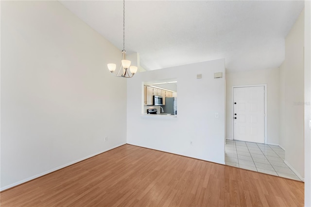 spare room with light wood-style flooring, a notable chandelier, and baseboards