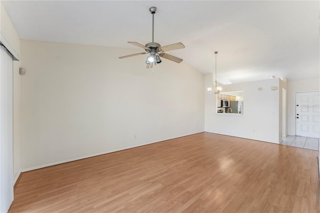 unfurnished living room with vaulted ceiling, ceiling fan with notable chandelier, and light wood finished floors