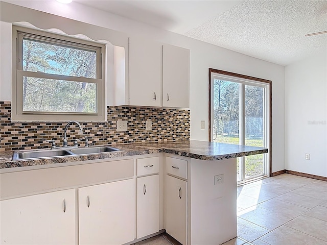 kitchen featuring a peninsula, white cabinets, tasteful backsplash, and a sink