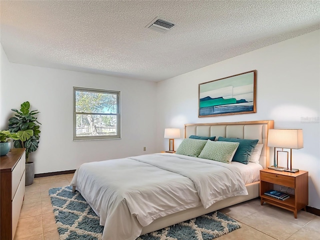 bedroom featuring light tile patterned flooring, visible vents, a textured ceiling, and baseboards