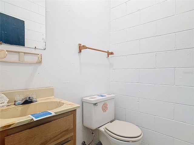 bathroom featuring vanity, concrete block wall, and toilet