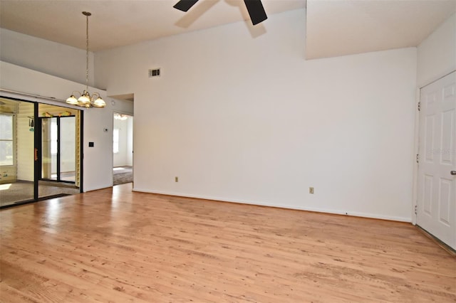 unfurnished room with visible vents, high vaulted ceiling, ceiling fan with notable chandelier, wood finished floors, and baseboards