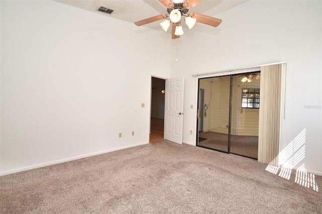 unfurnished bedroom with visible vents, baseboards, carpet, a towering ceiling, and a closet