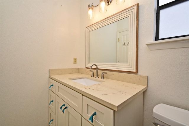 half bathroom featuring toilet, vanity, and a textured wall