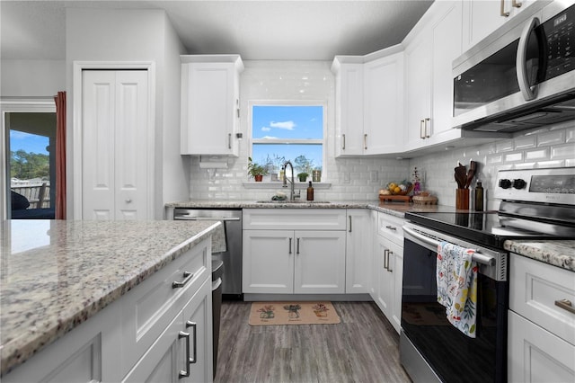 kitchen featuring dark wood-type flooring, a sink, stainless steel appliances, white cabinets, and decorative backsplash