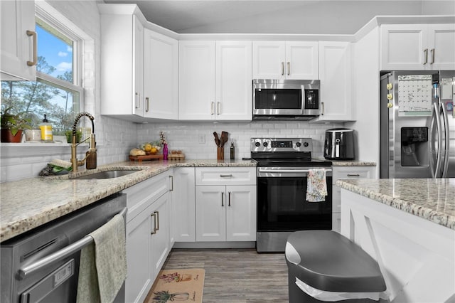 kitchen with lofted ceiling, a sink, decorative backsplash, appliances with stainless steel finishes, and white cabinetry