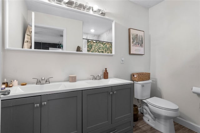 full bathroom featuring a shower with shower curtain, wood finished floors, double vanity, a sink, and toilet