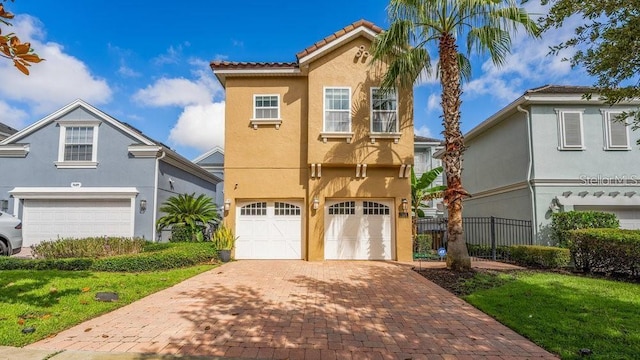 mediterranean / spanish-style home featuring stucco siding, an attached garage, decorative driveway, and fence