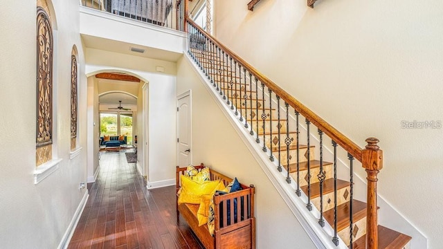 staircase with baseboards, visible vents, a high ceiling, arched walkways, and hardwood / wood-style flooring