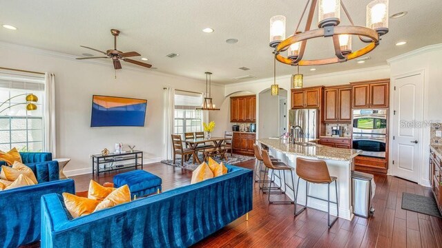 living room featuring dark wood-style floors, visible vents, baseboards, ornamental molding, and ceiling fan with notable chandelier