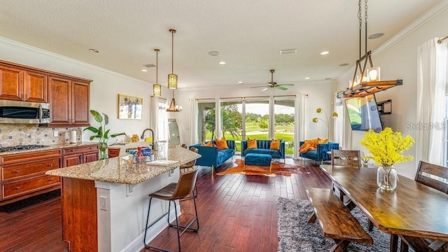 kitchen featuring open floor plan, stainless steel appliances, brown cabinetry, light stone countertops, and dark wood-style flooring