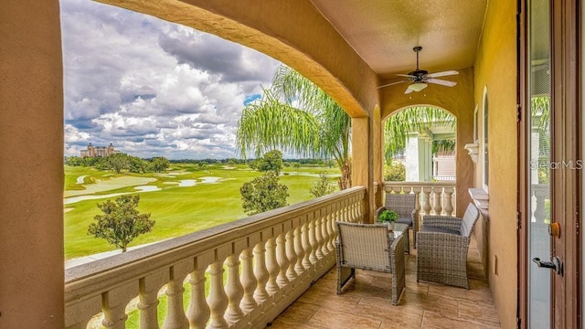 balcony with view of golf course and a ceiling fan