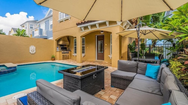 view of swimming pool with fence, exterior kitchen, a pool with connected hot tub, an outdoor living space with a fire pit, and a patio area