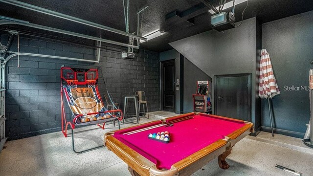 rec room with concrete block wall, pool table, concrete floors, and a garage