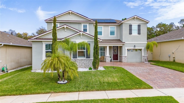 craftsman-style house with a front lawn, roof mounted solar panels, decorative driveway, stone siding, and an attached garage