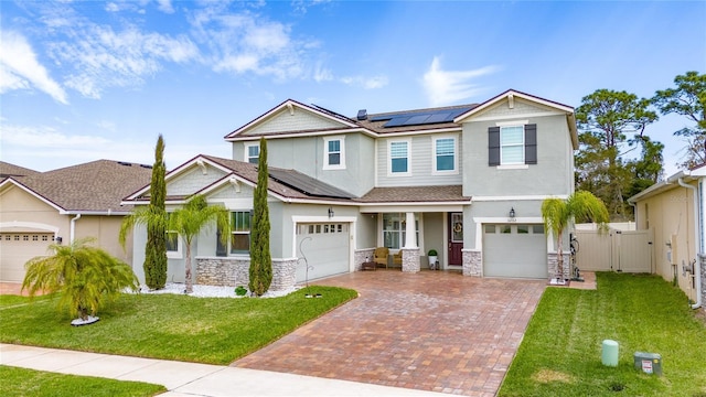 craftsman-style house featuring decorative driveway, stone siding, roof mounted solar panels, fence, and a front yard