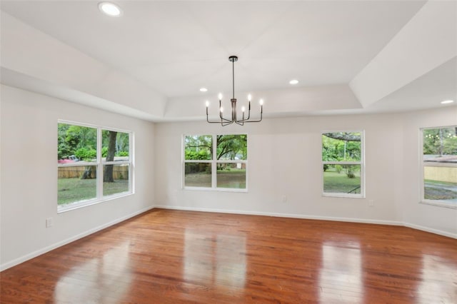 empty room featuring a notable chandelier, a raised ceiling, baseboards, and wood finished floors