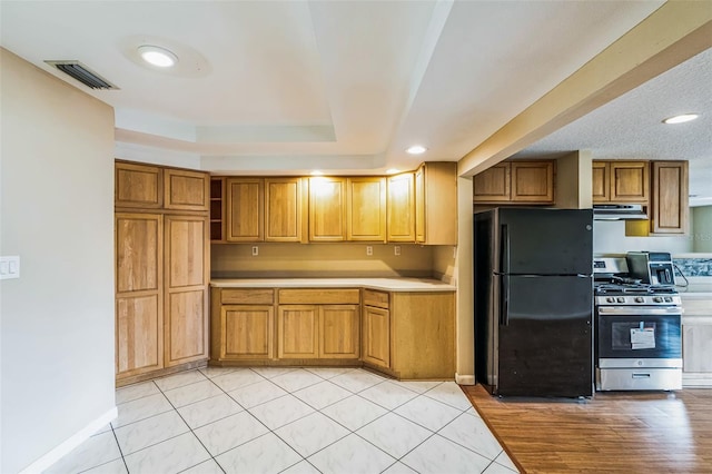 kitchen featuring visible vents, freestanding refrigerator, ventilation hood, stainless steel range with gas cooktop, and light countertops