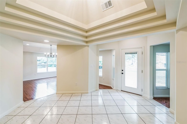 entrance foyer featuring light tile patterned floors, baseboards, visible vents, a tray ceiling, and a chandelier