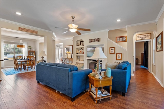 living room with dark wood-style floors, built in features, ceiling fan, and ornamental molding