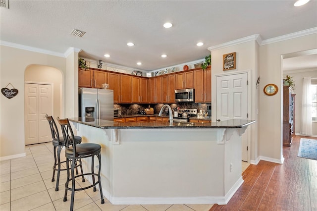 kitchen featuring visible vents, ornamental molding, decorative backsplash, stainless steel appliances, and a kitchen bar