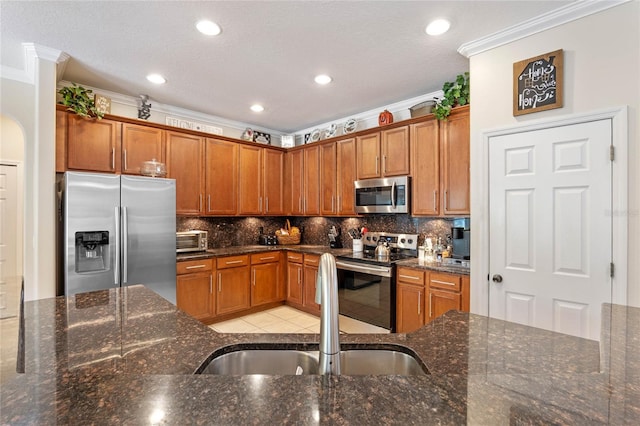 kitchen with brown cabinets, a sink, appliances with stainless steel finishes, crown molding, and tasteful backsplash