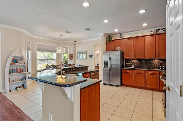 kitchen with a sink, arched walkways, appliances with stainless steel finishes, and brown cabinets