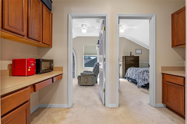 kitchen featuring brown cabinetry, light colored carpet, built in desk, and black microwave