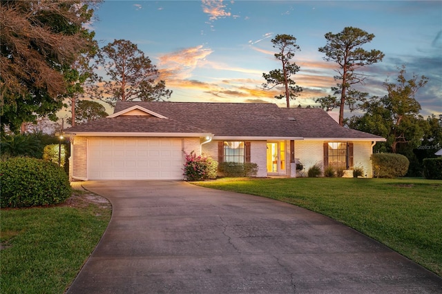 ranch-style house with driveway, a yard, a shingled roof, a garage, and brick siding