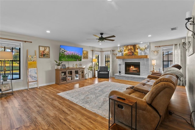 living room featuring visible vents, baseboards, a brick fireplace, and wood finished floors