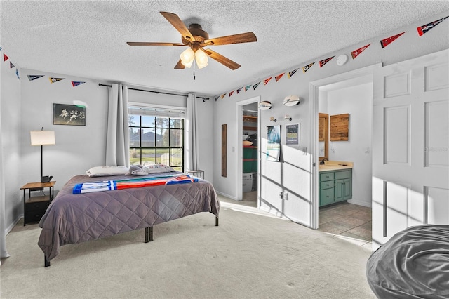 bedroom featuring a ceiling fan, light colored carpet, ensuite bathroom, and a textured ceiling