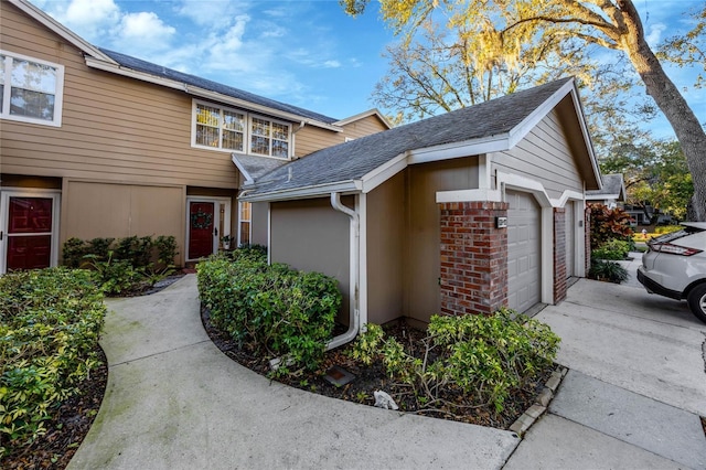 view of property exterior with an attached garage, brick siding, driveway, and a shingled roof