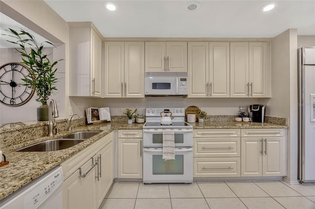 kitchen with a sink, light stone counters, recessed lighting, white appliances, and light tile patterned flooring