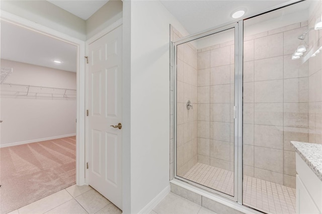 full bathroom with a shower stall, a walk in closet, baseboards, tile patterned floors, and vanity