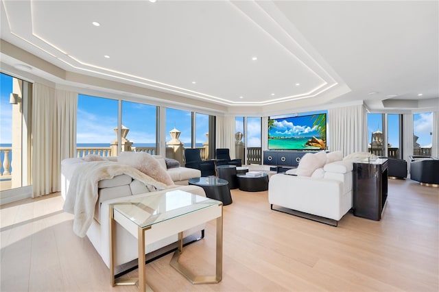 living room with recessed lighting, a raised ceiling, and light wood-style flooring