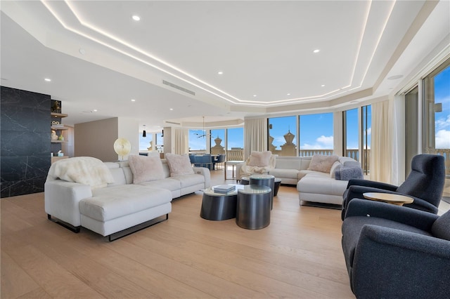 living room featuring recessed lighting, a tray ceiling, and light wood finished floors