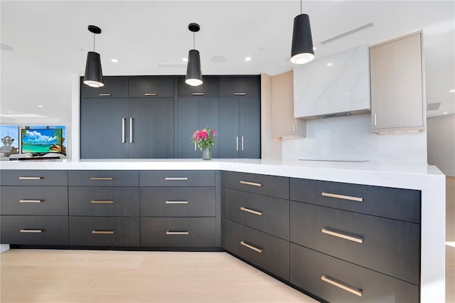 kitchen featuring light countertops, light wood-style flooring, hanging light fixtures, modern cabinets, and wall chimney exhaust hood