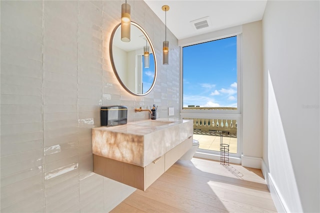 bathroom featuring vanity, wood finished floors, visible vents, tile walls, and toilet