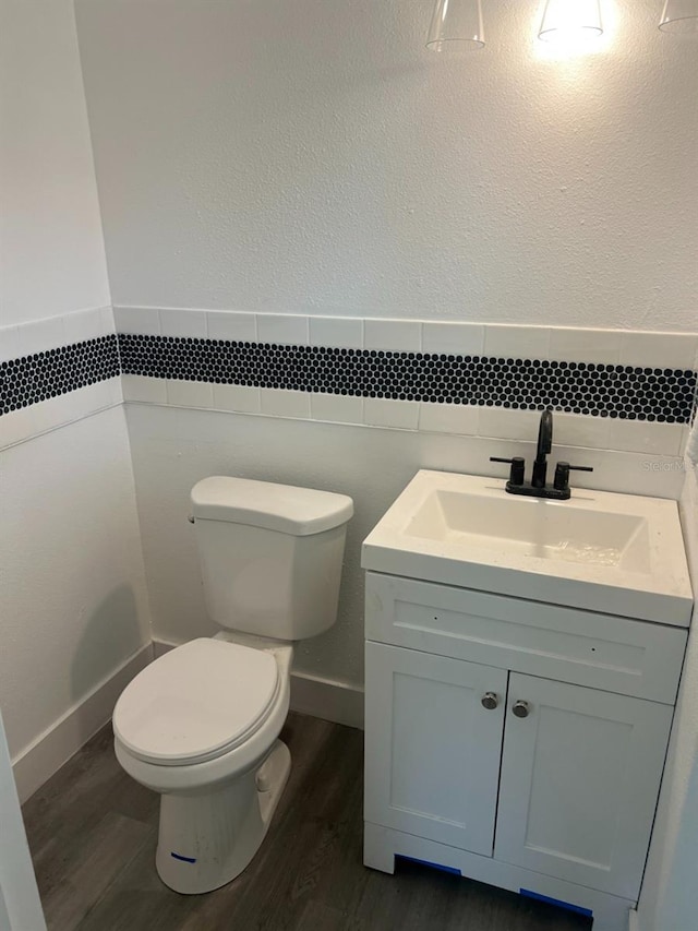 half bathroom featuring a wainscoted wall, toilet, wood finished floors, a textured wall, and vanity