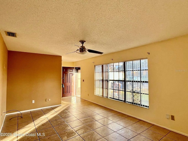 spare room featuring tile patterned flooring, visible vents, baseboards, a textured ceiling, and a ceiling fan