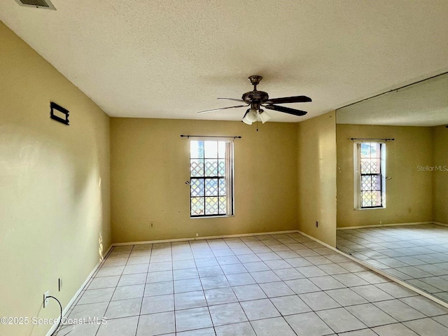 spare room featuring light tile patterned floors, a ceiling fan, visible vents, baseboards, and a textured ceiling