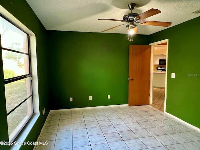 spare room featuring visible vents, a textured ceiling, light tile patterned floors, baseboards, and ceiling fan