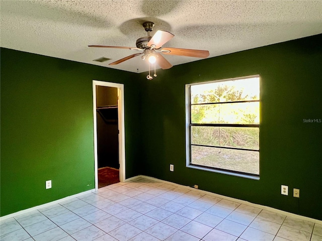 empty room featuring visible vents, baseboards, ceiling fan, light tile patterned floors, and a textured ceiling