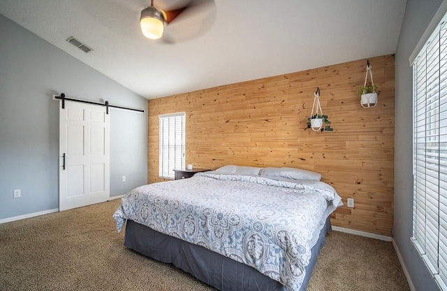 carpeted bedroom featuring wooden walls, visible vents, ceiling fan, a barn door, and vaulted ceiling