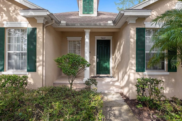 entrance to property featuring stucco siding and a shingled roof