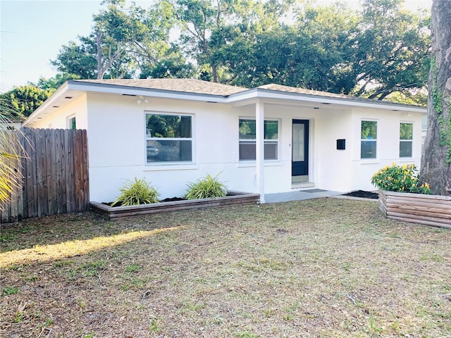 view of front of house with stucco siding, a front yard, and fence