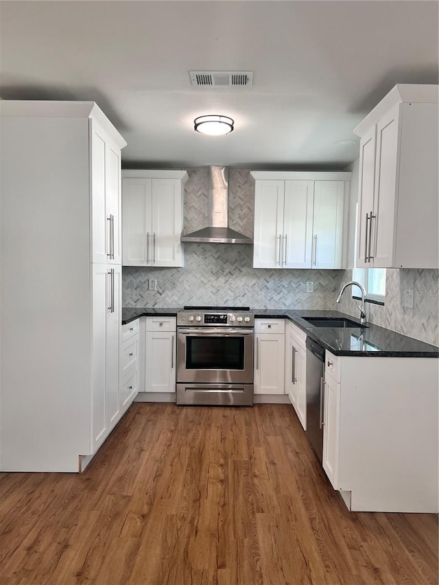 kitchen featuring visible vents, wall chimney range hood, wood finished floors, stainless steel appliances, and a sink