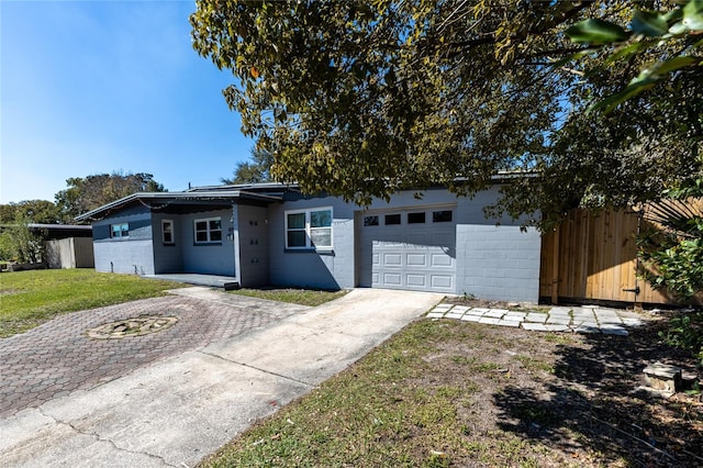 view of front of house featuring an attached garage, fence, a front yard, concrete block siding, and driveway